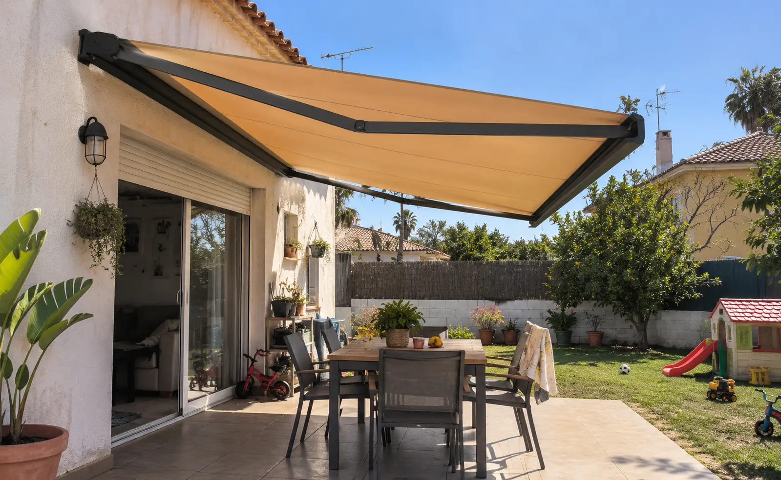Toldo motorizado beige desplegado sobre un comedor exterior con jardín