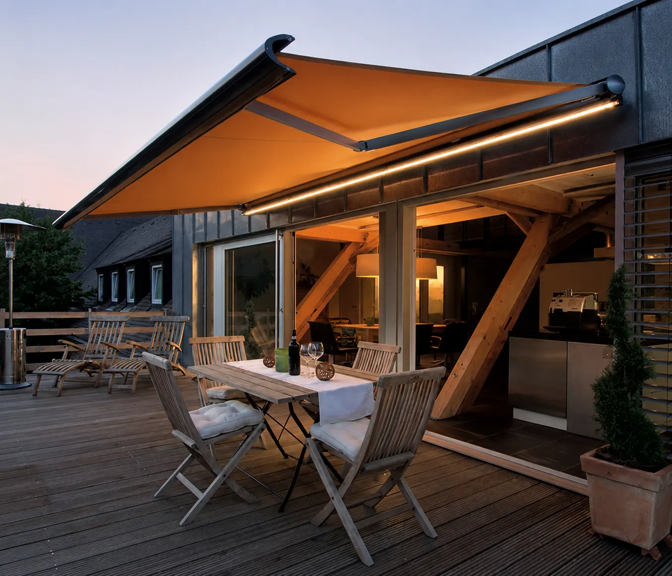 Toldo cofre con luces LED encendidas sobre una terraza de madera al atardecer