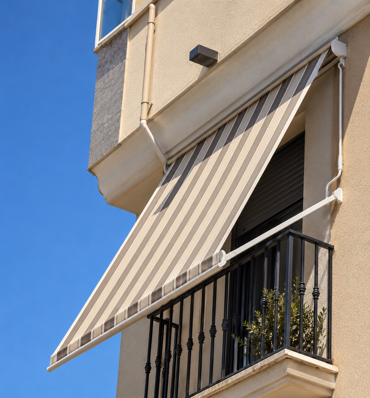 Toldo punto recto de rayas beige y gris en balcón con barandilla negra