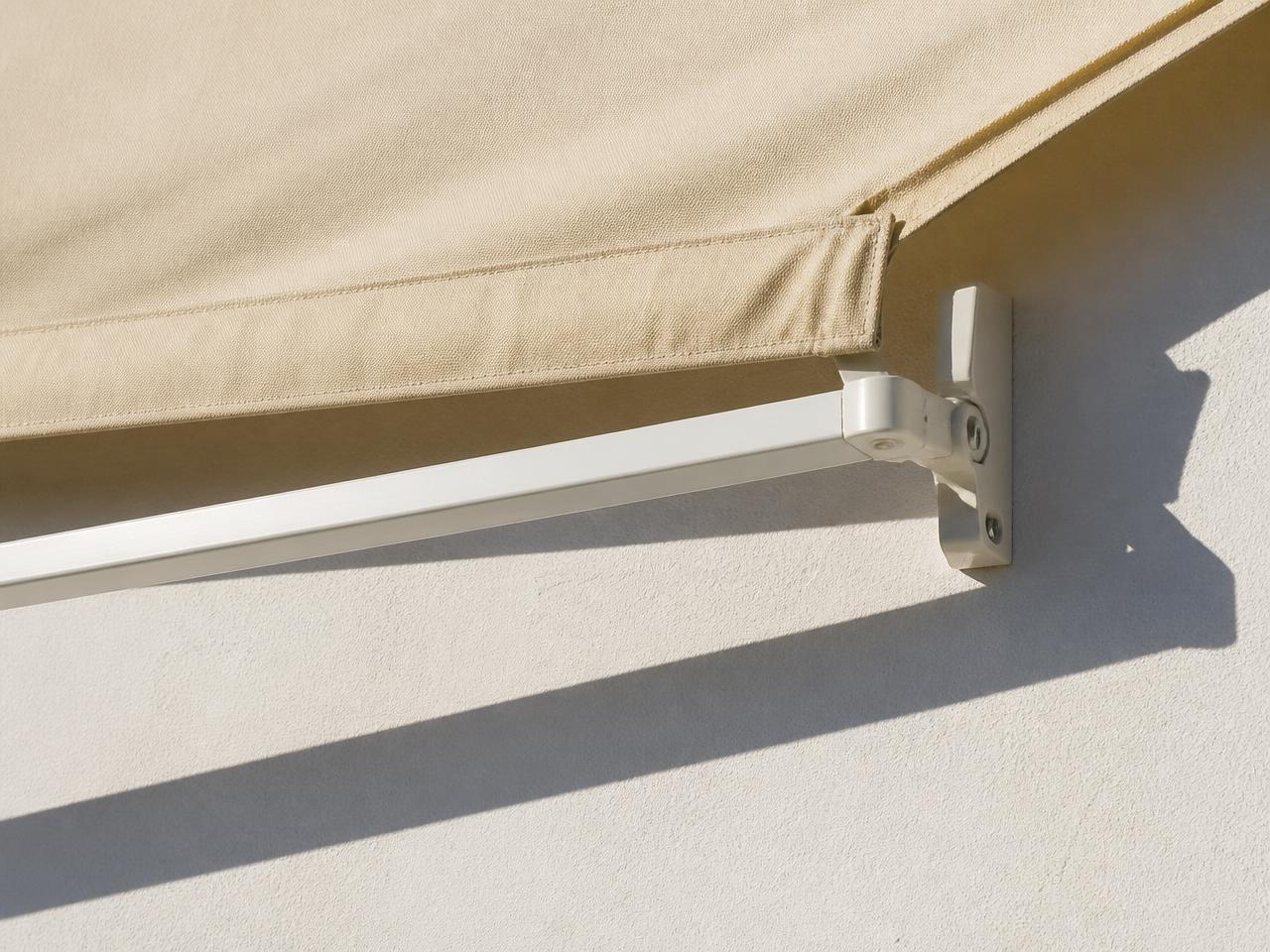 Detalle del brazo y la lona de un toldo sobre pared blanca