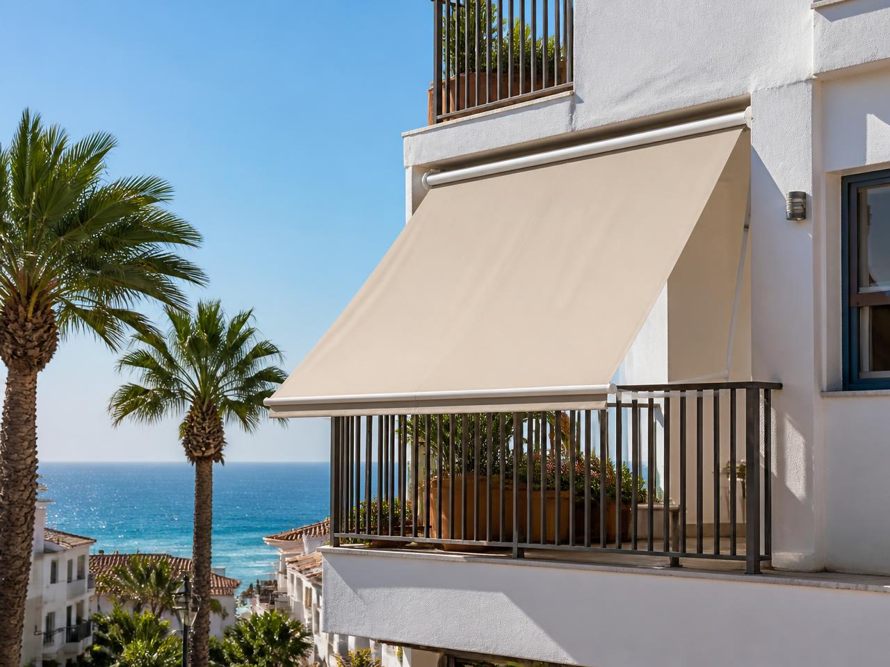 Toldo store beige instalado en un balcón, con la lona apoyada en la barandilla y vistas al mar